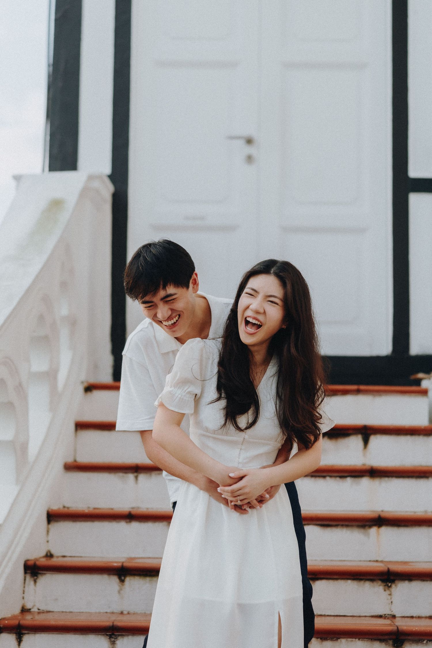 A couple shares a candid moment of laughter on white steps.
