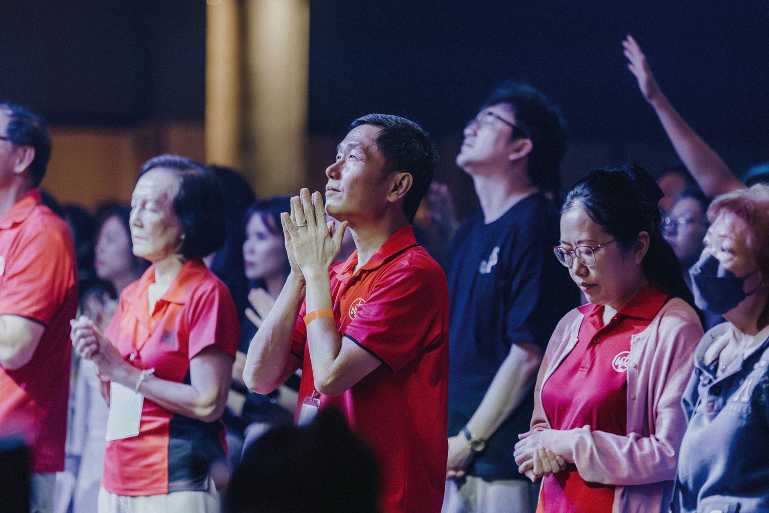 A crowd of people wearing red shirts gathered in prayer at a public event.