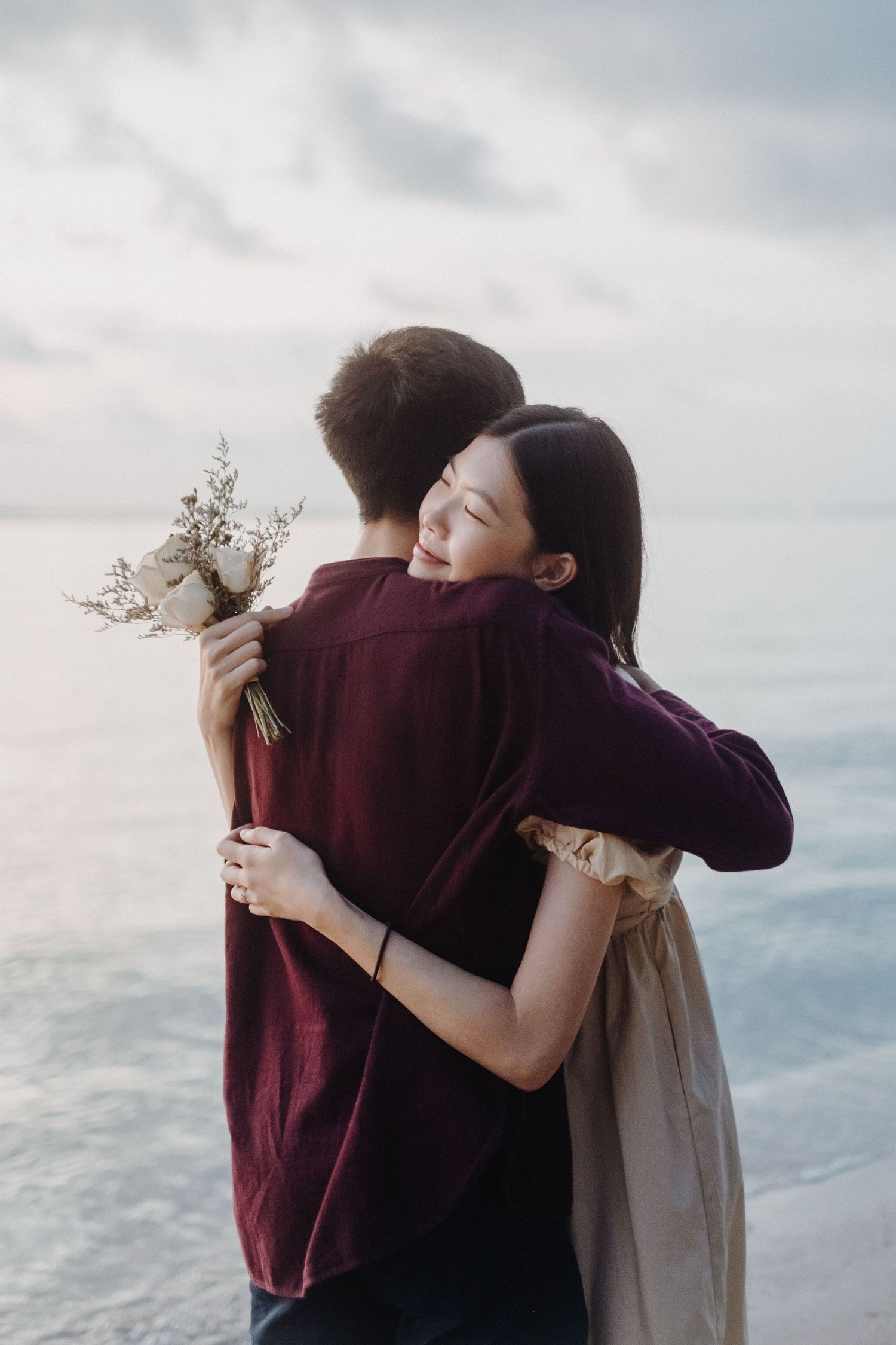 A couple embraces tenderly on a cloudy beach during a romantic moment.