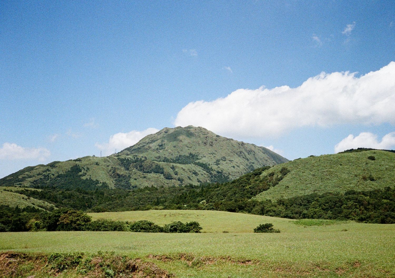 Rolling green hills and mountains under blue sky with scattered white clouds.