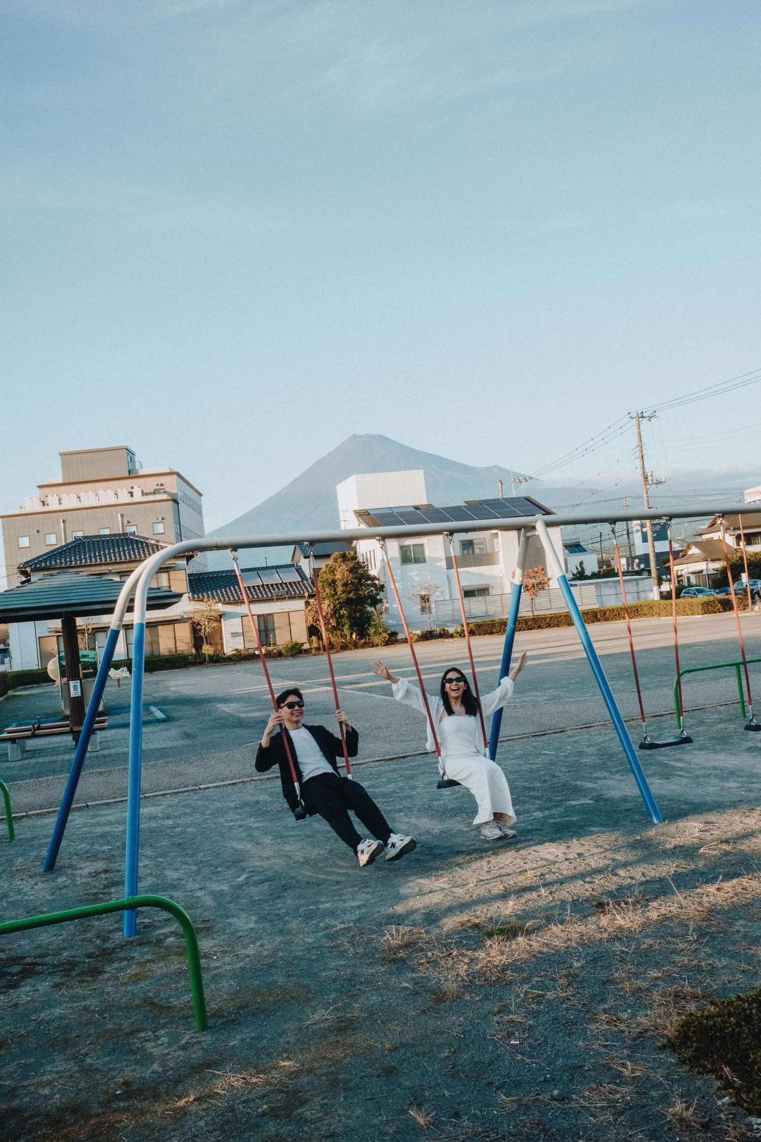 Two people swinging together on playground swings against a mountain backdrop.