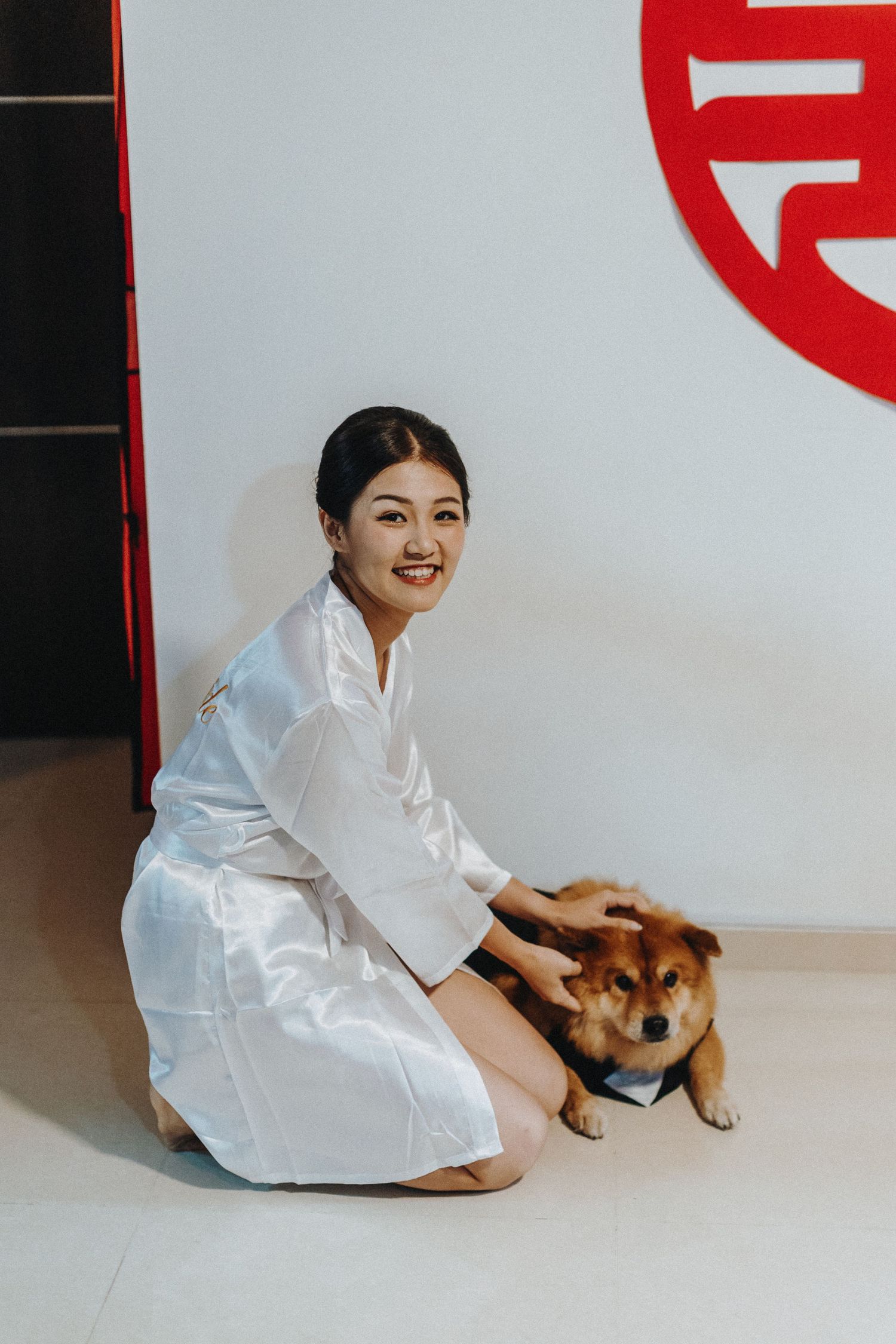 A person in white silk attire sits with a brown dog on the floor.
