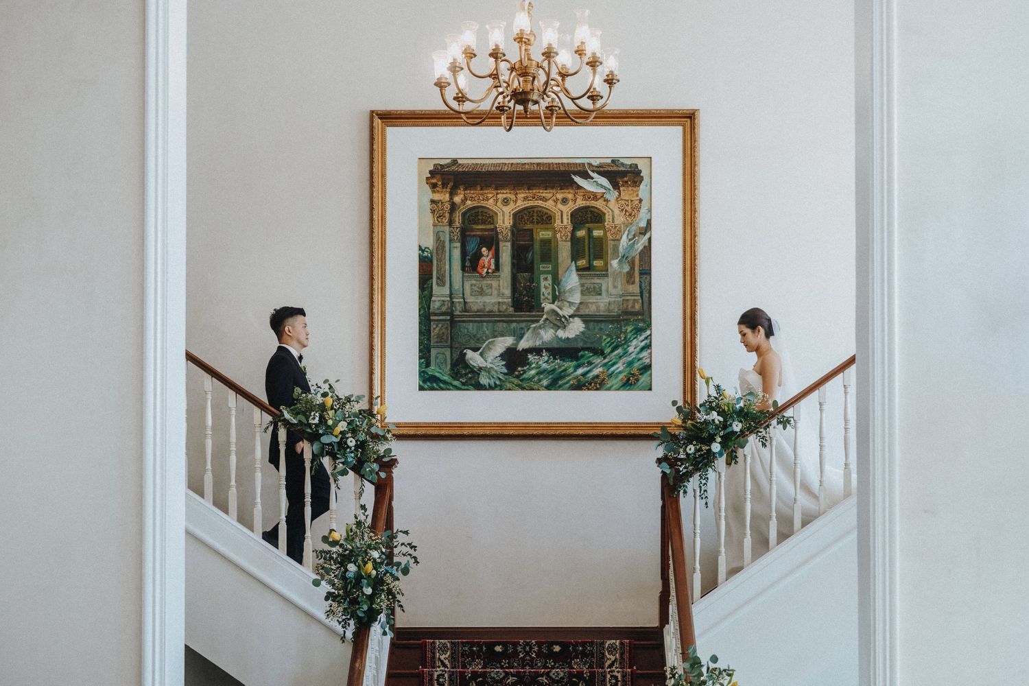 A grand staircase decorated with greenery and florals featuring a large framed artwork and elegant chandelier.