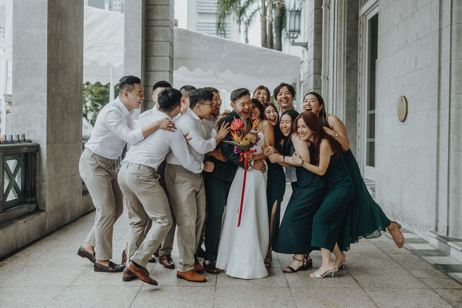 Wedding party poses playfully together in a corridor with bridesmaids in green dresses and groomsmen in light suits.