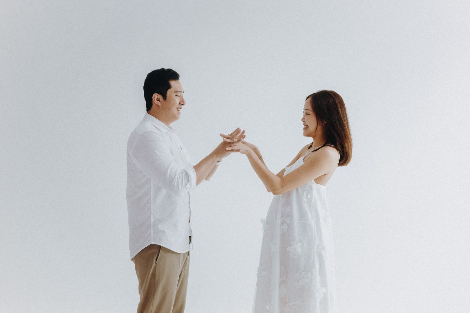 Couple in white clothes sharing tender moments together in a minimalist white studio setting.