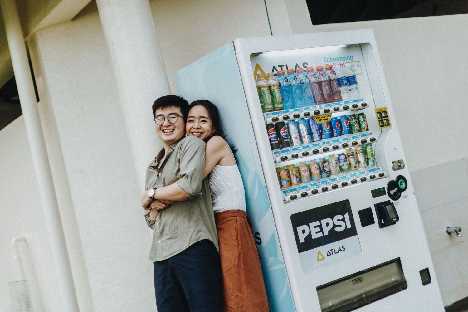 A series of vending machines line a wall with people standing near them and passing by.