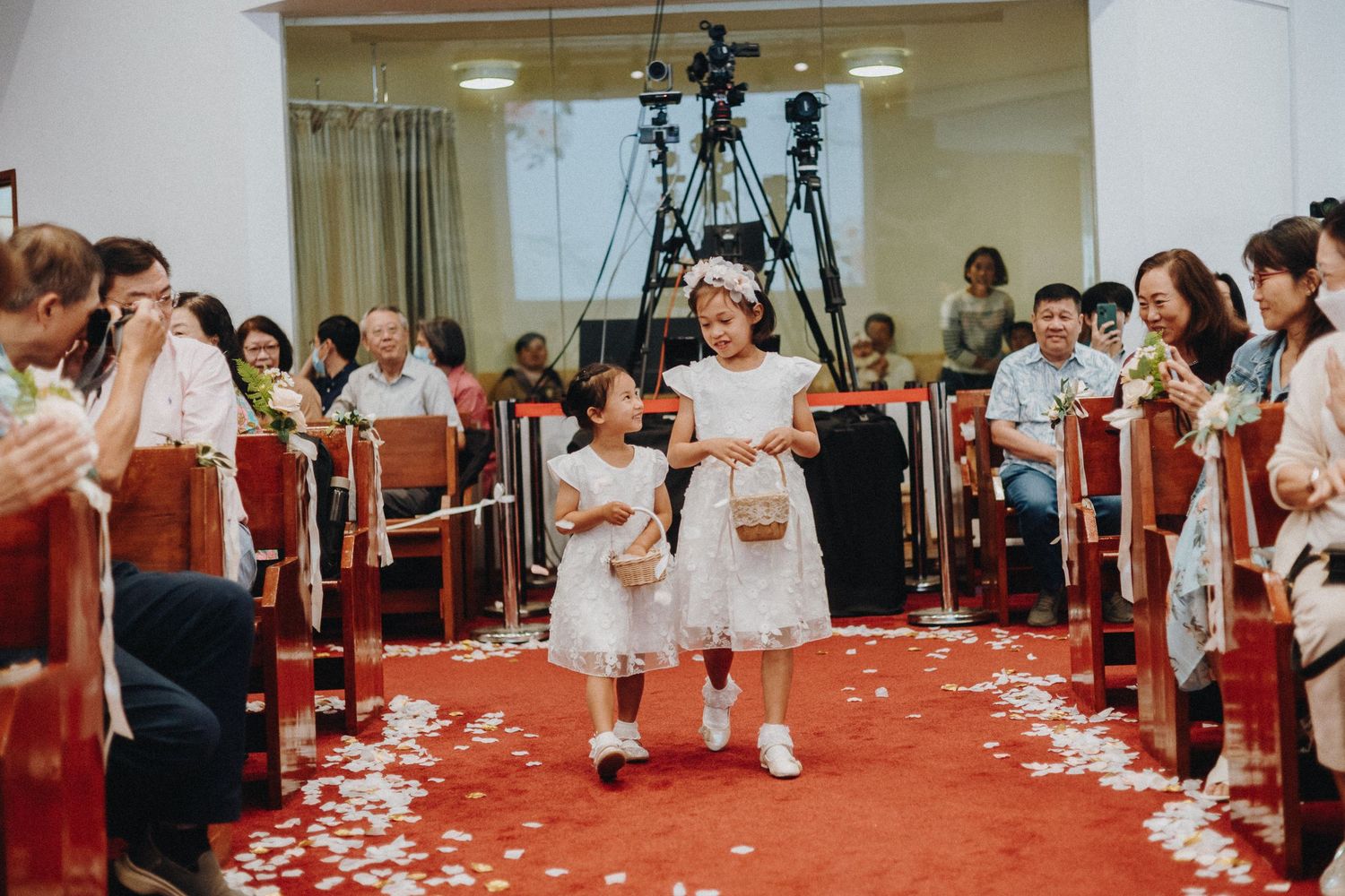 Wedding guests throw petals and celebrate in church aisle with red carpet.