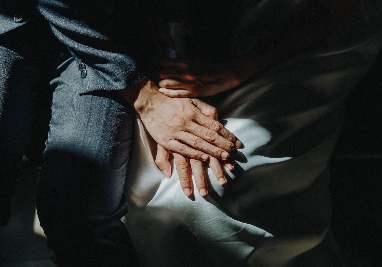 Close-up shot of hands clasped together in dramatic lighting against a dark background.