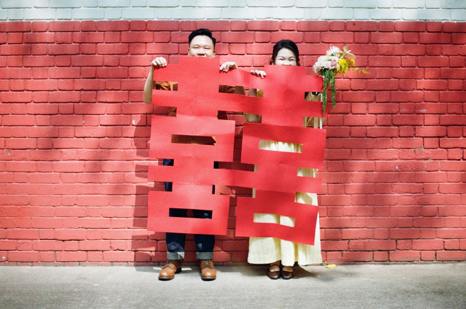A creative wedding photo with a red double happiness symbol wall backdrop in an urban setting.