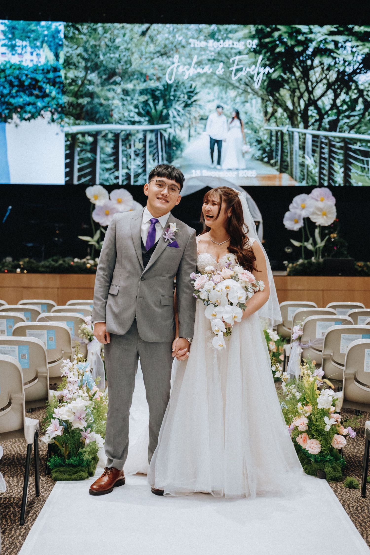 Wedding ceremony setup outdoors with white chairs and floral arrangements along a tree-lined path.