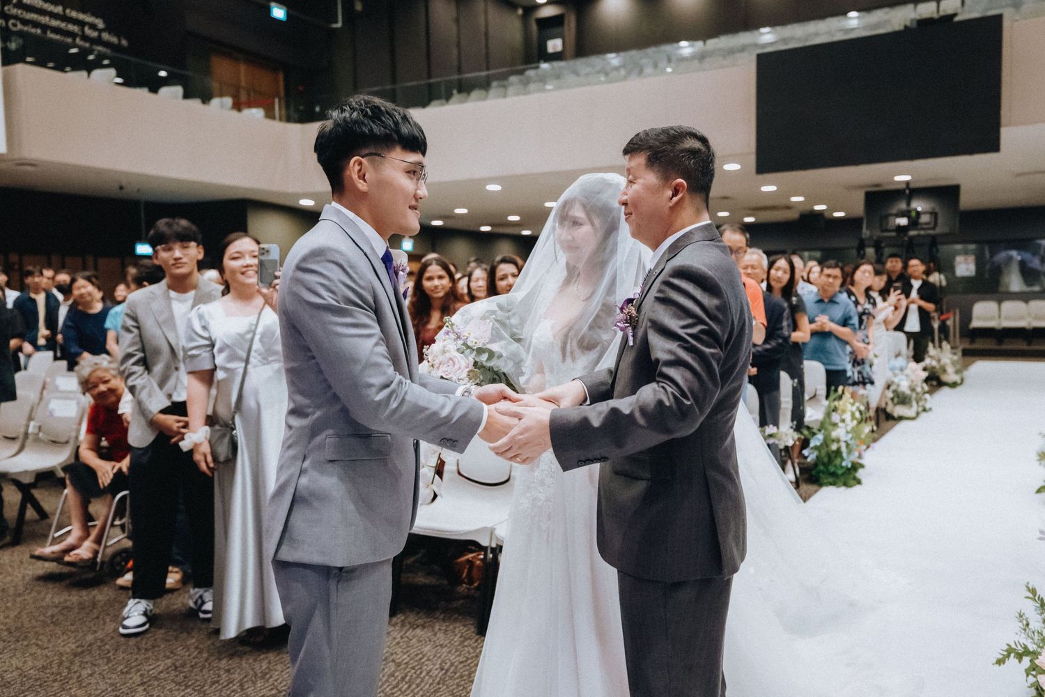 A wedding ceremony in progress with attendees watching the couple exchange vows in a modern indoor venue.