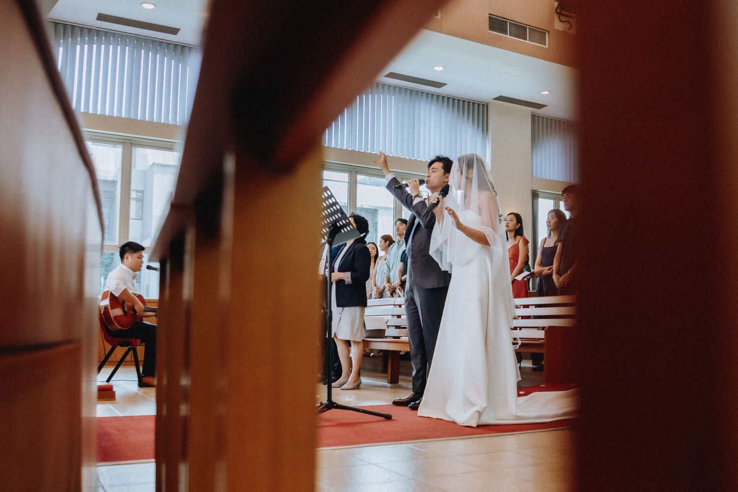 Bride and groom sharing first dance viewed through wooden church pews.
