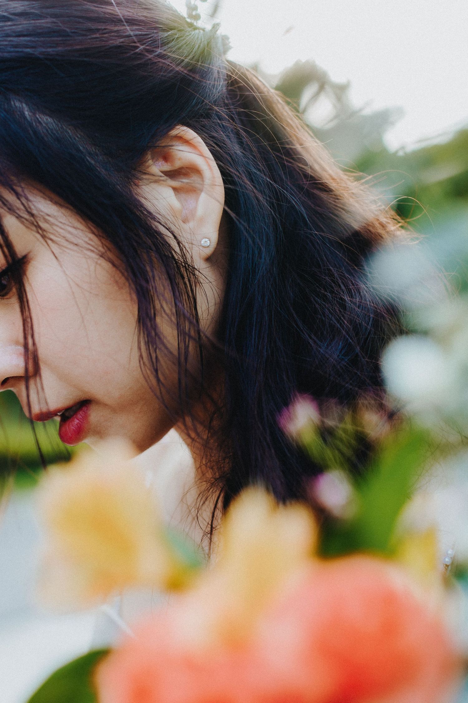 Close-up artistic photo of black hair against blurred coral and yellow flowers in garden setting.