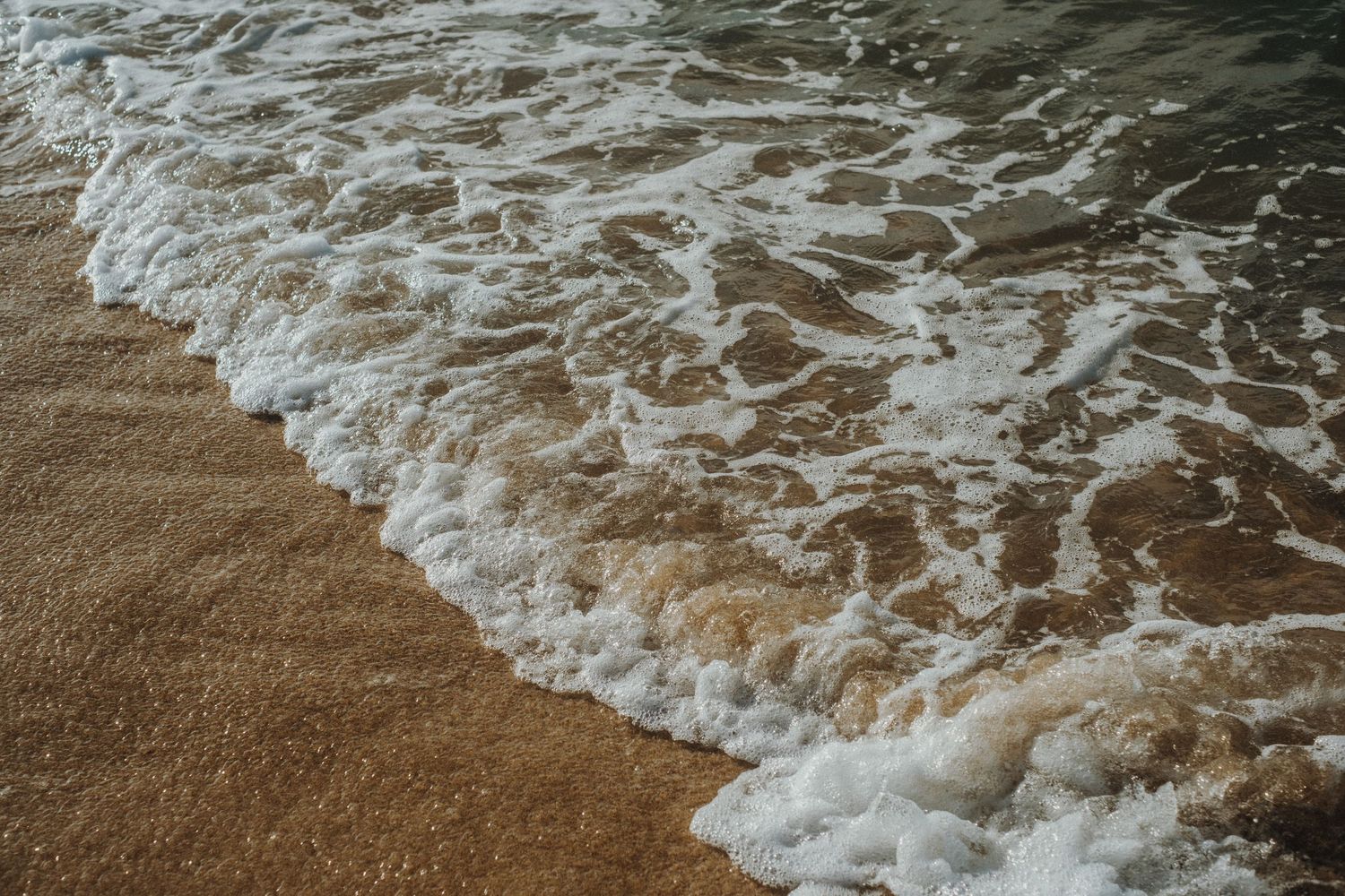 Ocean waves washing up on sandy beach during sunset with golden tones.