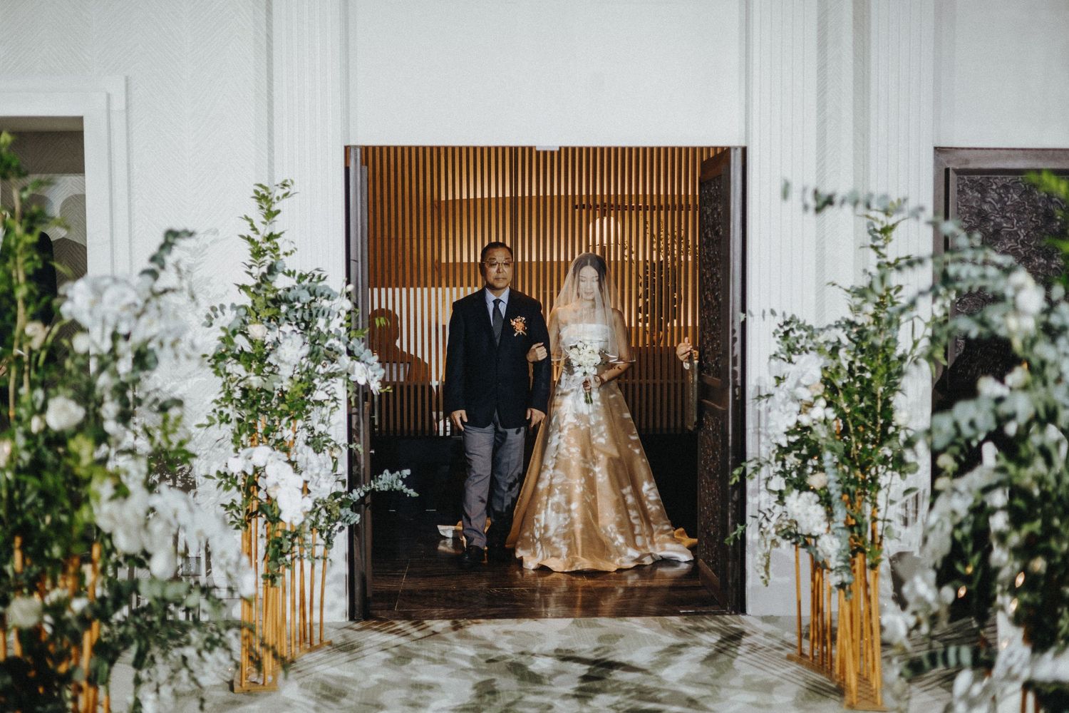 Elegant wedding ceremony setup with white floral arrangements and wooden accents in a modern indoor venue.
