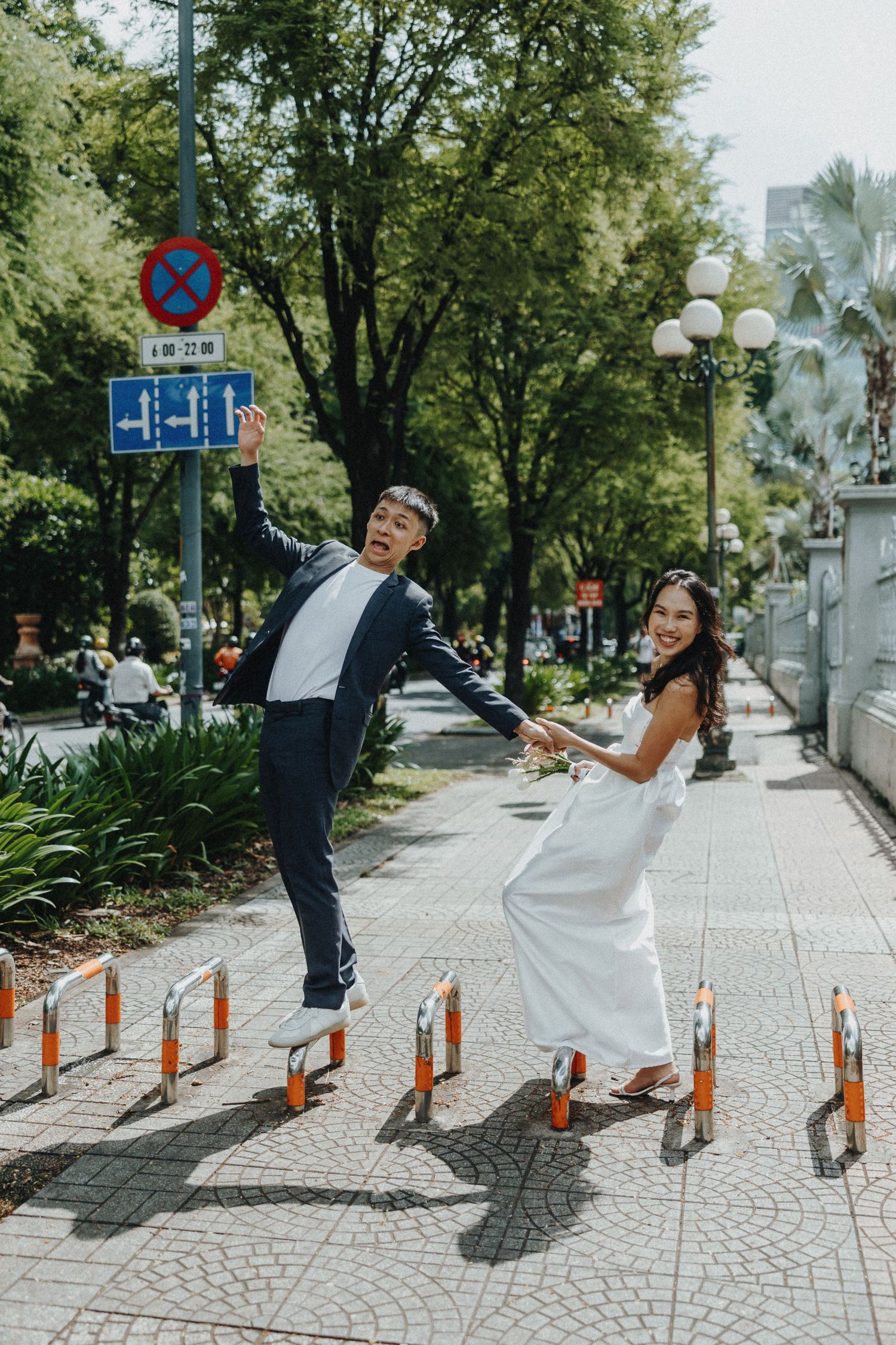 Couple doing creative jumping dance poses on a patterned stone pathway lined with orange traffic posts.