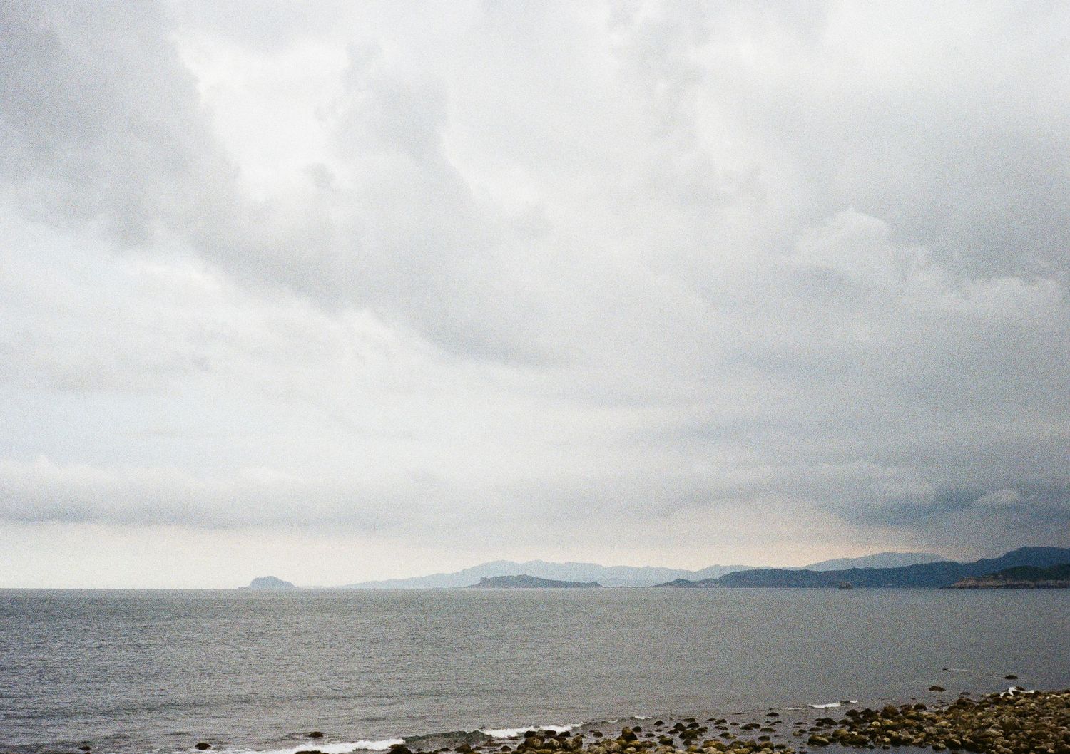 Cloudy ocean panorama with rocky coastline and distant mountains on the horizon.