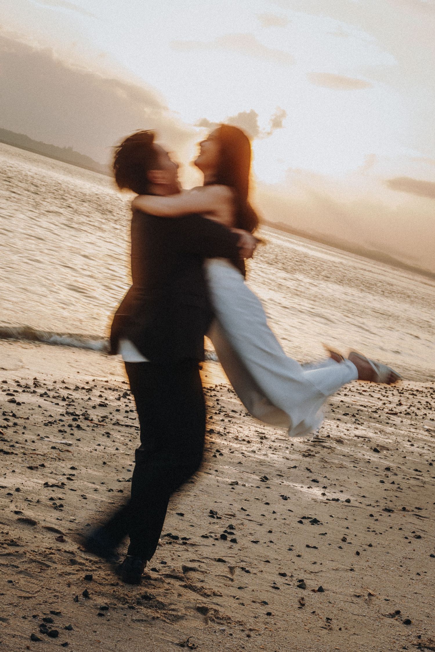 Motion-blurred couple spinning in dance on beach with sunset glow.
