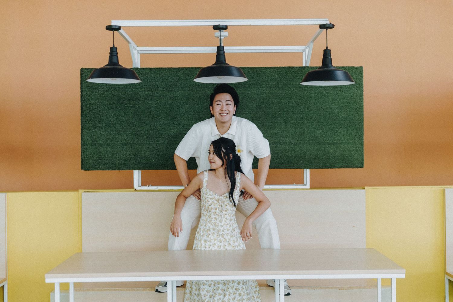 Couple having fun posing together in front of green chalkboard wall and pendant lights.