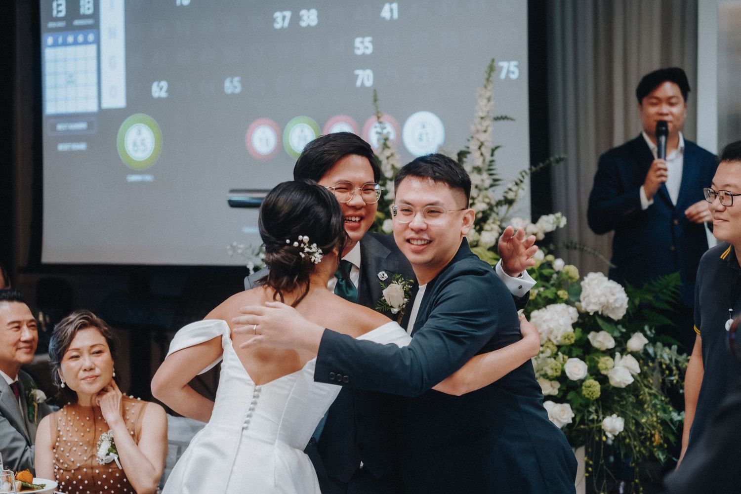 Joyful celebration at a wedding reception with floral decorations and projected display.