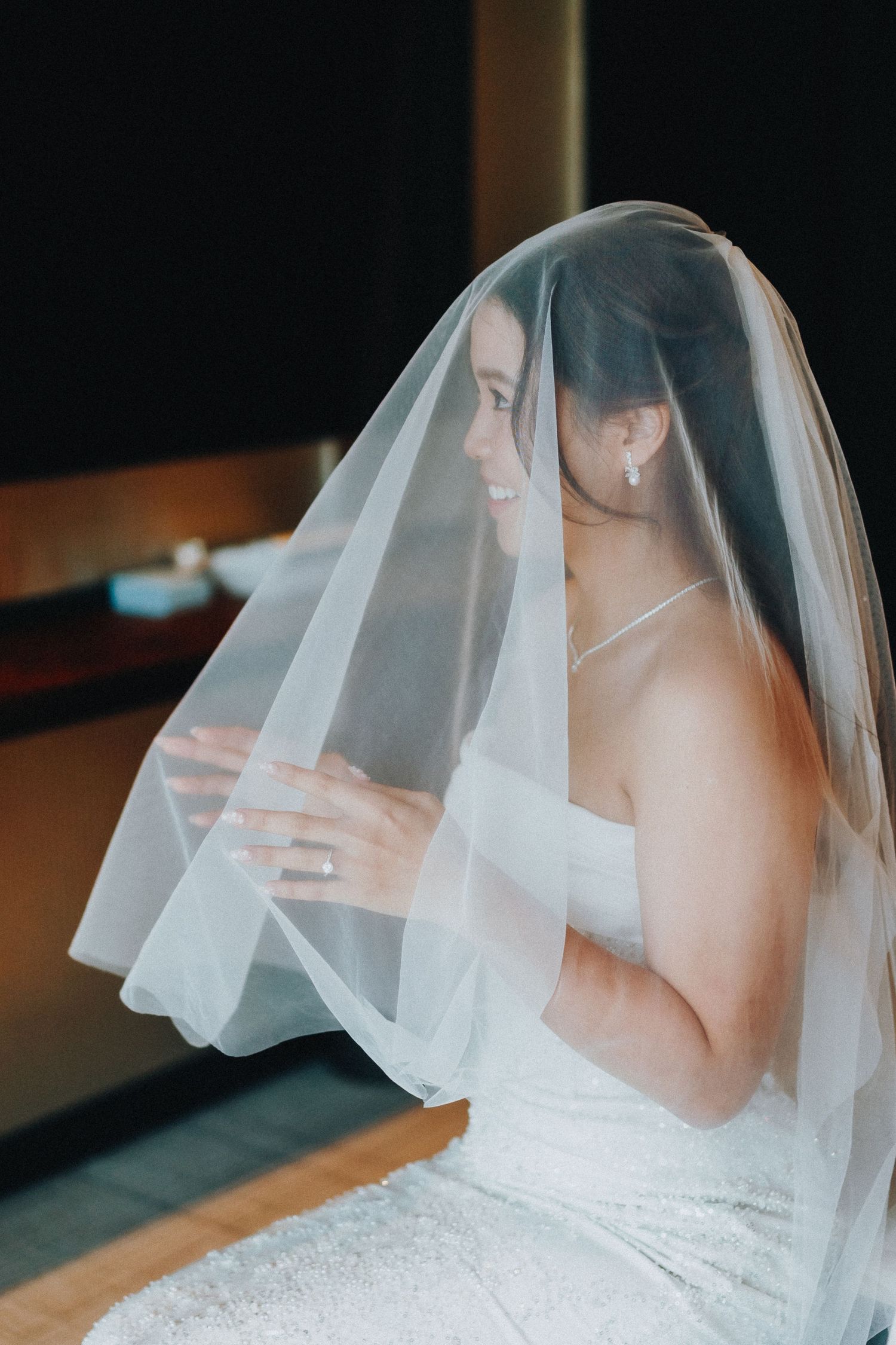 Bride in white wedding dress and veil poses elegantly during wedding preparation.