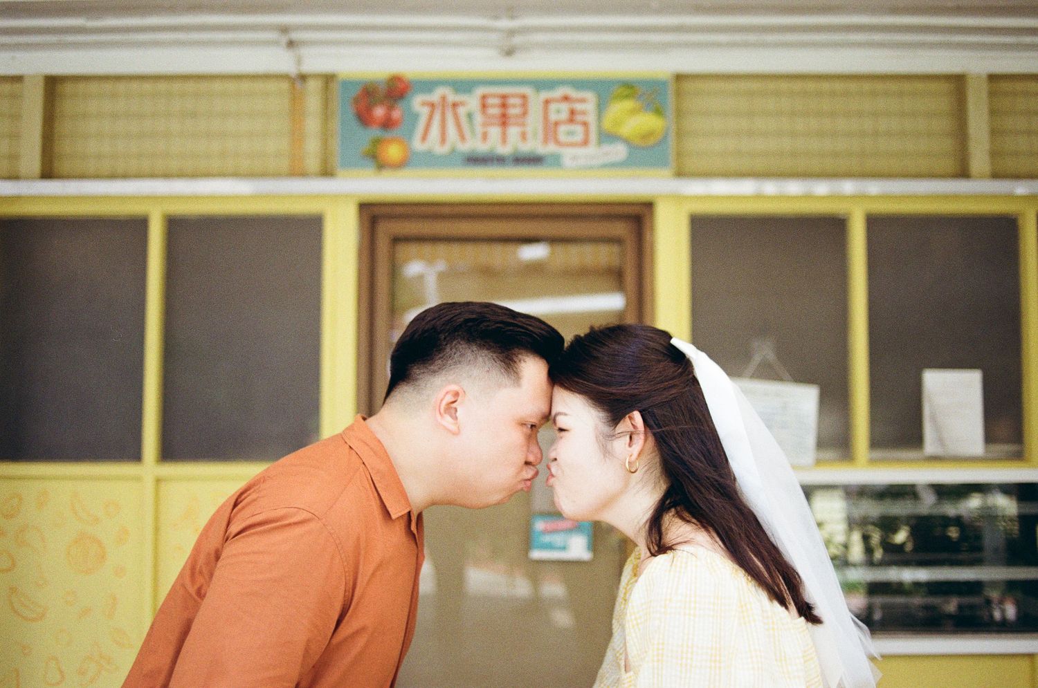 A couple sharing a romantic moment in front of an Asian storefront with Chinese characters on the sign.