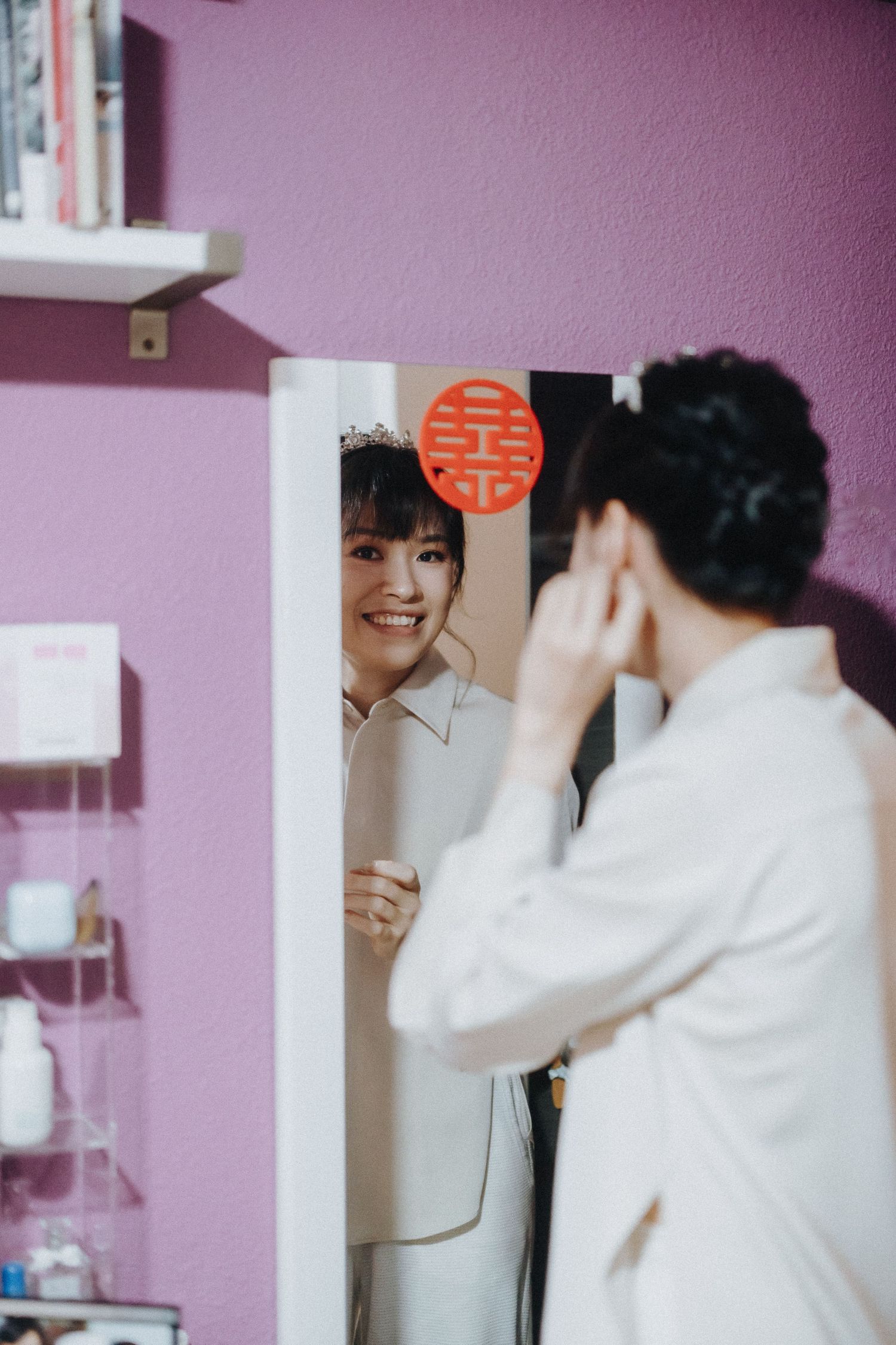 Wedding preparation scene showing joyful moments with a traditional double happiness symbol on a pink wall.