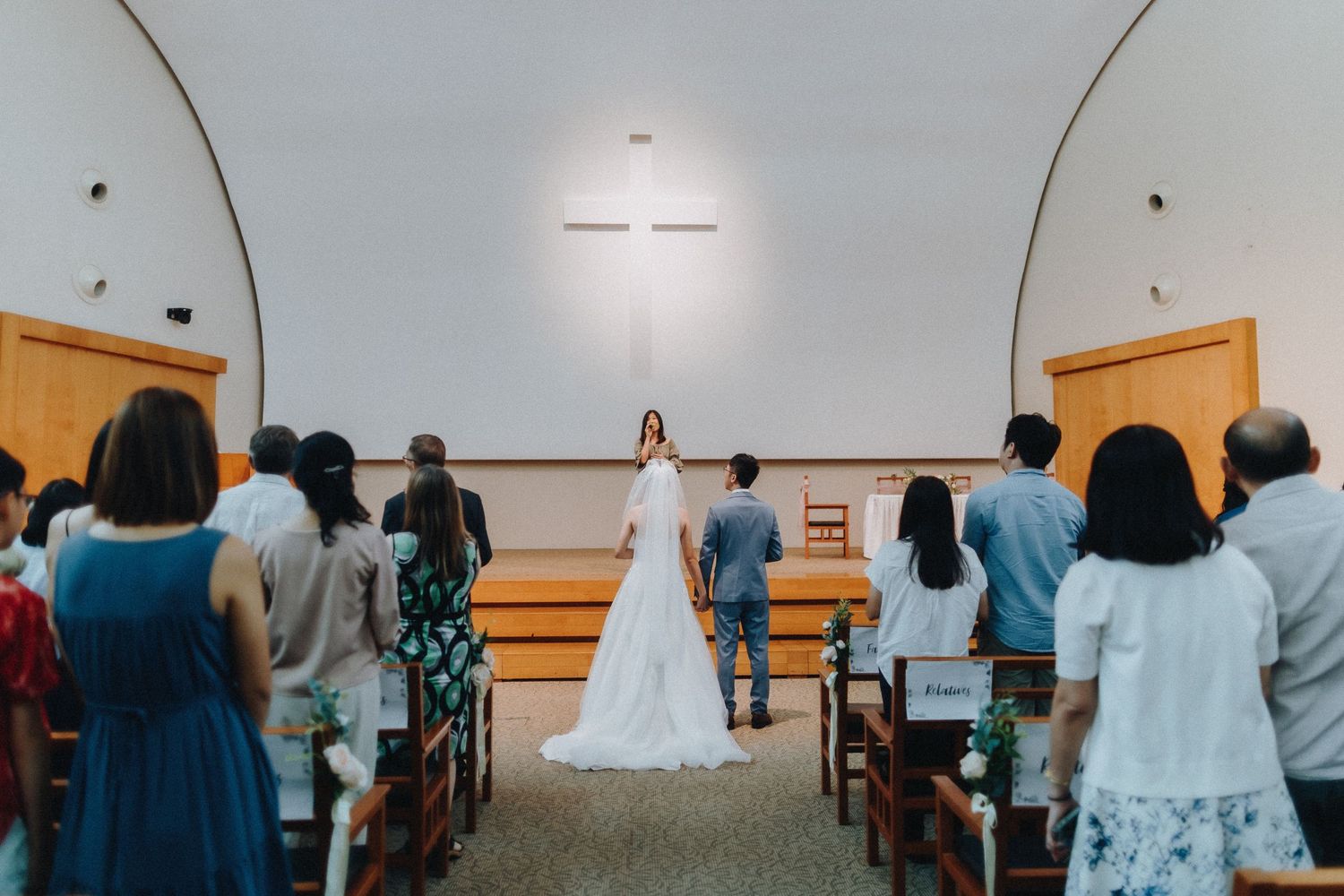 Wedding ceremony in progress with guests seated in rows inside a minimalist church setting.