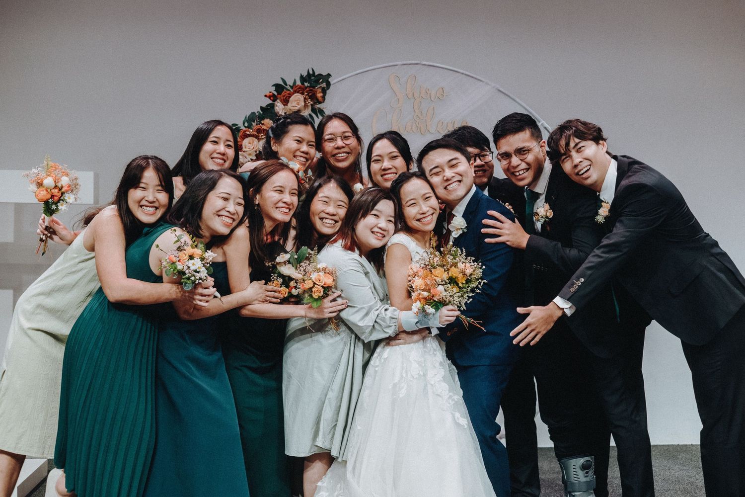 Wedding party members laugh and pose together in a fun group photo along church pews.