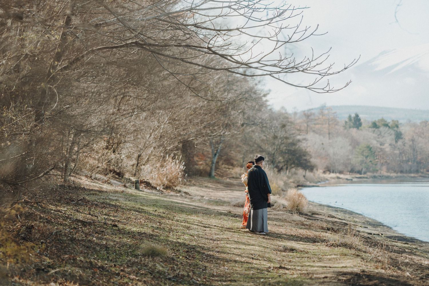 Scenic lakeside path with bare trees and mountains visible in the distance.