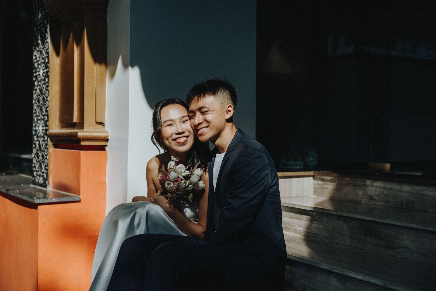 A candid moment of joy and laughter captured outside a building with an orange wall in natural lighting.