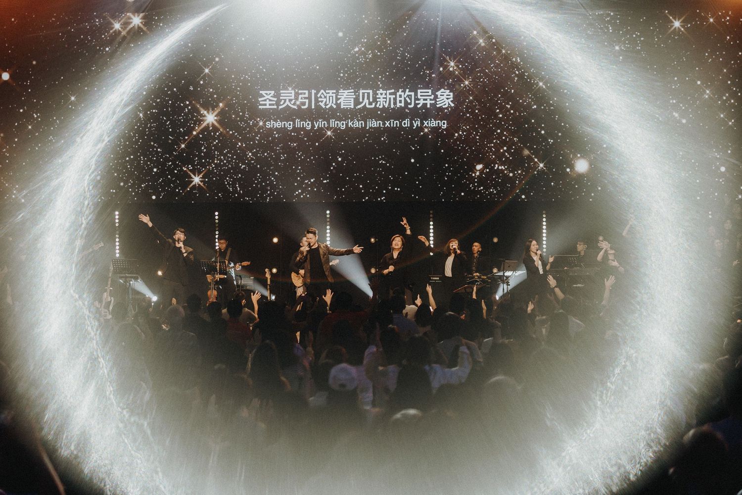 Concert crowd silhouetted beneath a glowing circular light effect with Chinese text overlay.