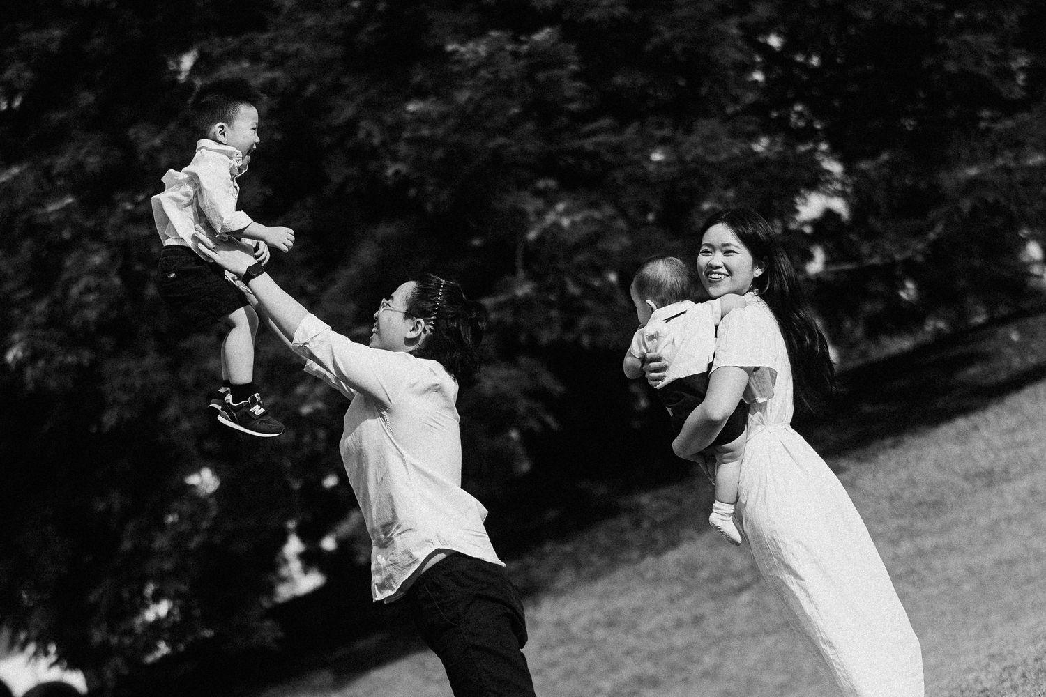 A vintage black and white photograph captures playful moments between adults and children in a garden setting.