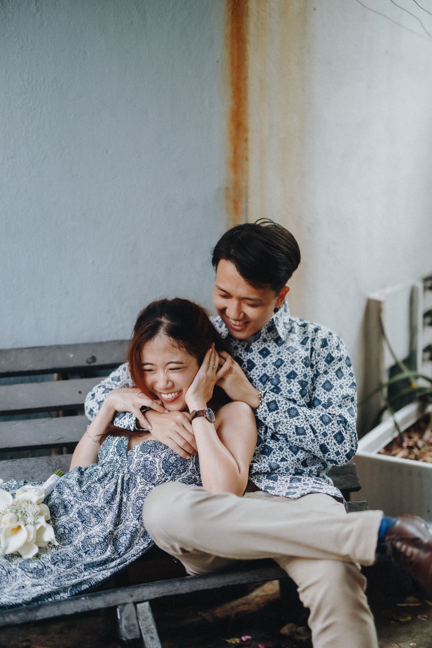 Two people in matching blue and white floral tops share playful moments while lounging together on a couch.