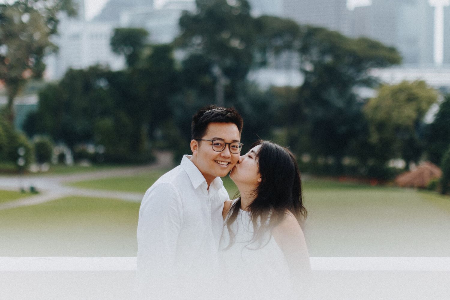 A romantic couple shares an intimate moment while standing outdoors with city buildings in background.
