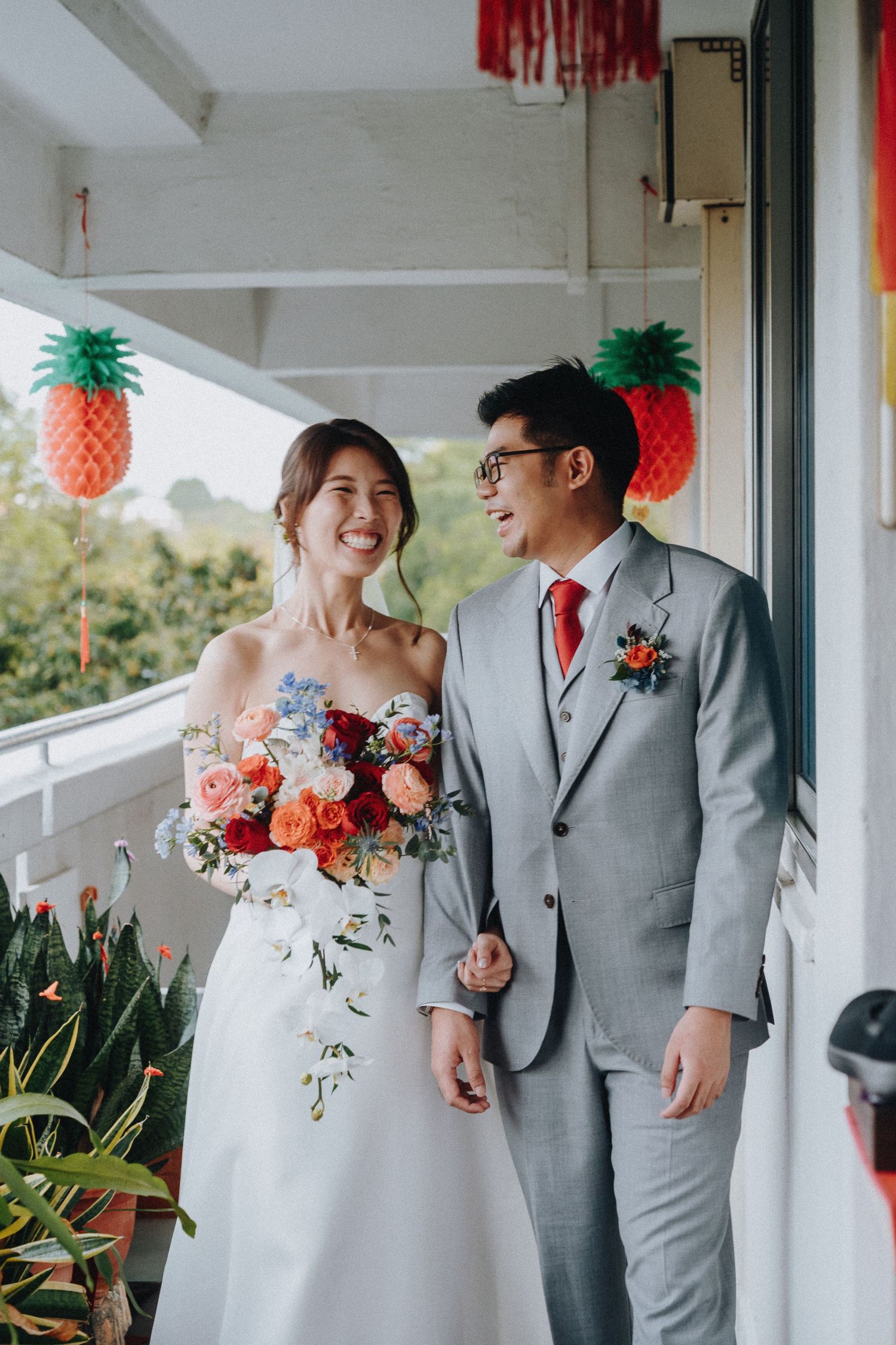 Wedding portrait with decorative pineapple lanterns and colorful bouquet on a balcony.