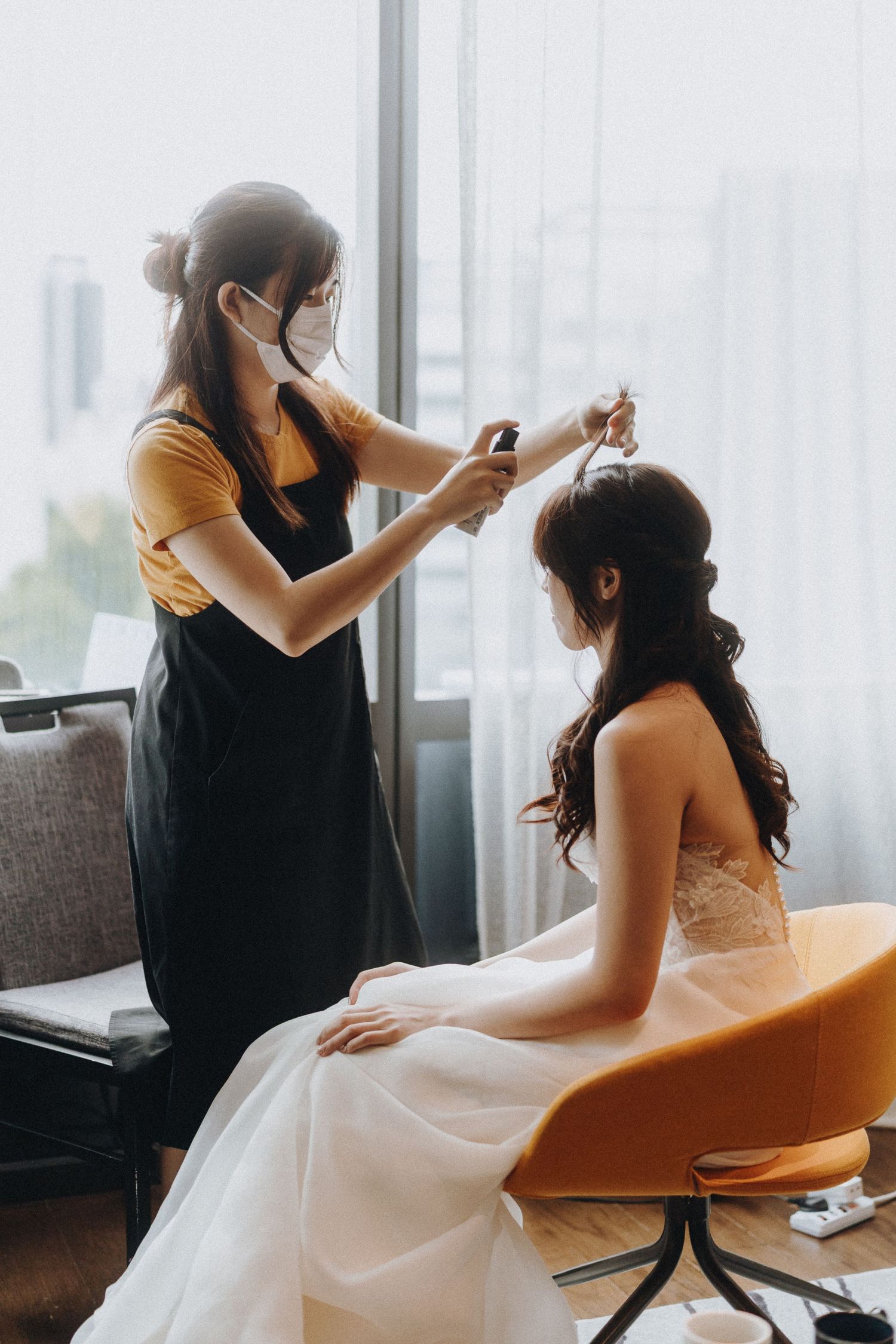 A stylist works on final wedding preparations, adjusting details for a bride seated in an elegant white gown.