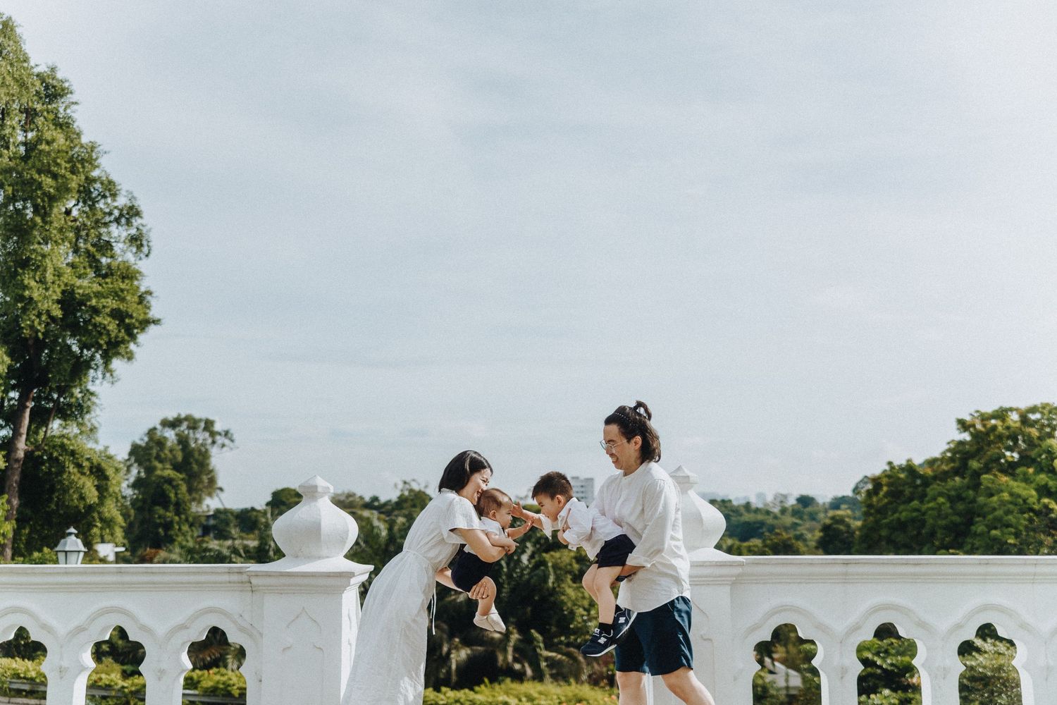 Two people playing with a dog on a sunny day beside a white railing at an outdoor venue.