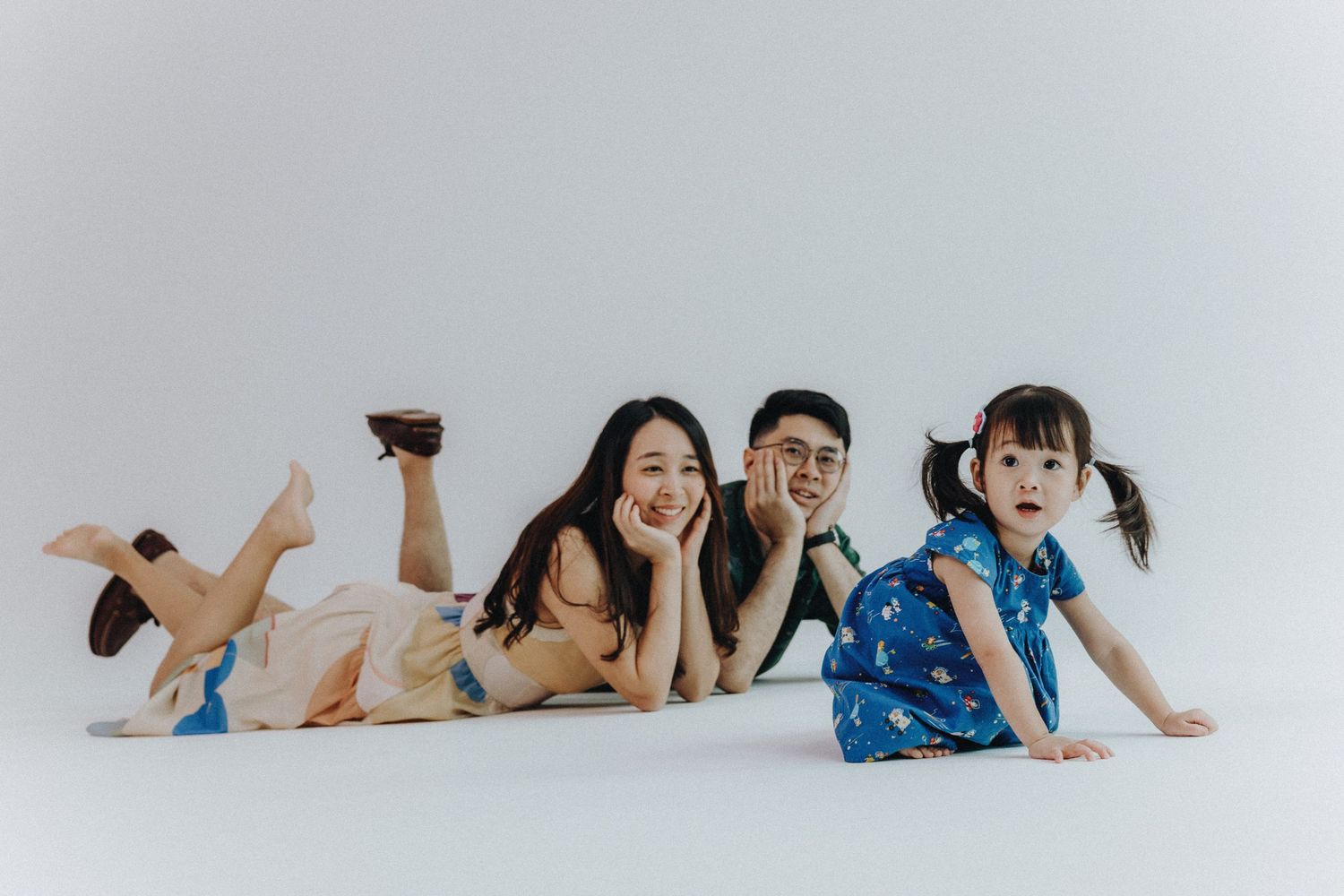 Family lying on floor in casual pose for playful studio portrait.