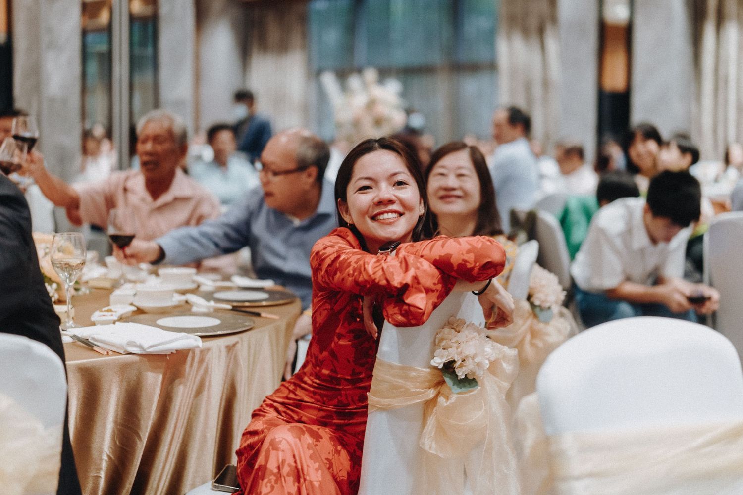 A person in a red traditional Chinese qipao dress celebrating joyfully at a wedding reception banquet.