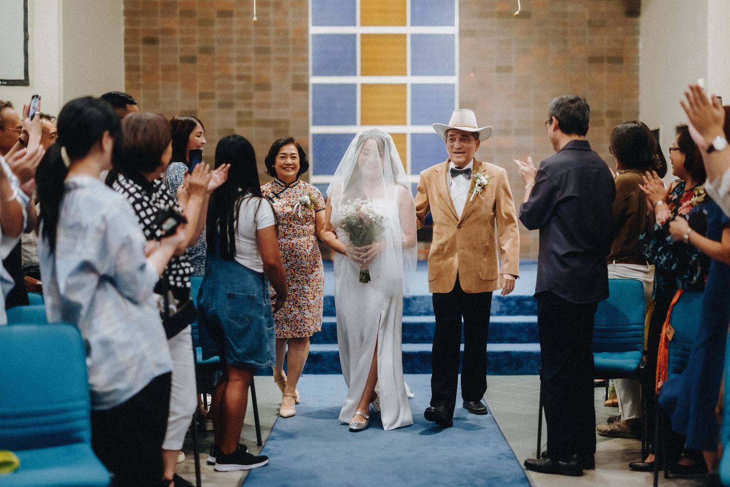Wedding party and guests celebrating in a church with blue carpet and brick walls.