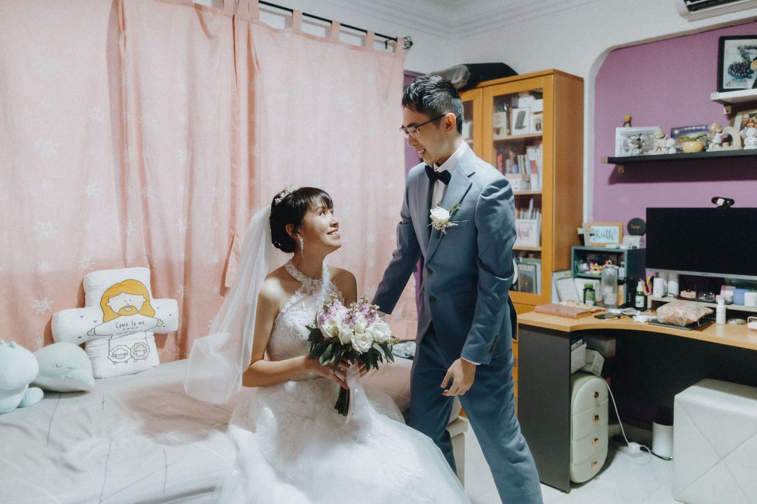 A couple shares a joyful moment in a bedroom setting with pink walls on their wedding day.