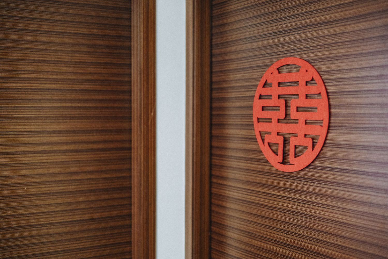Red circular double happiness symbol mounted on brown wooden paneled wall in Asian-inspired interior design.