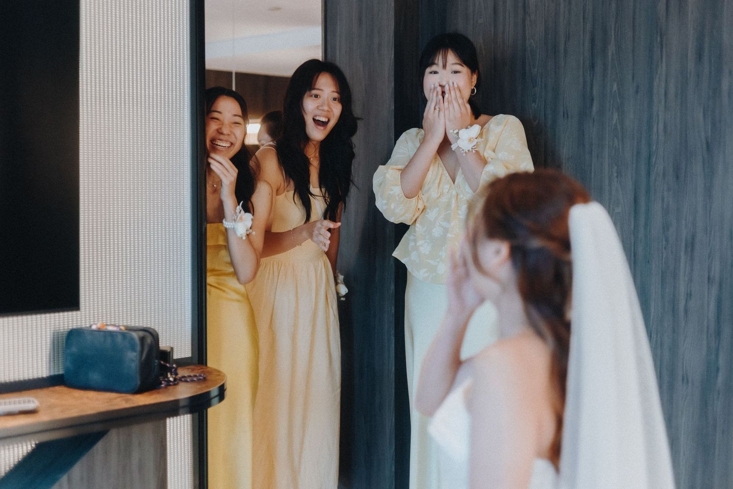 Bridesmaids in pastel dresses share an emotional moment with a bride in white at a wedding venue.