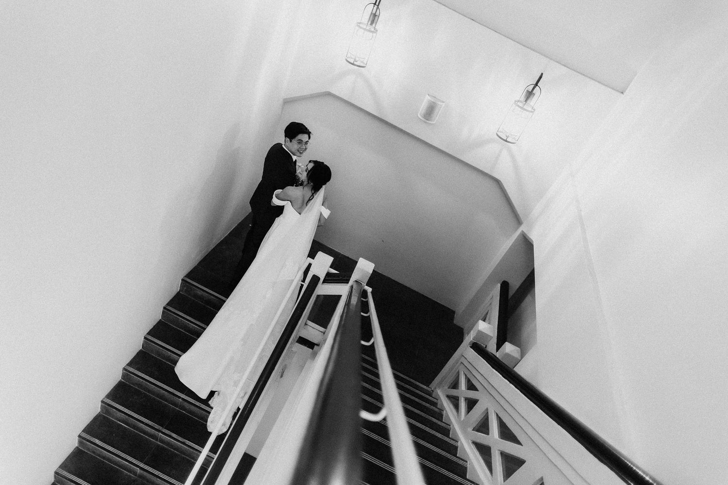 Black and white photograph of a couple ascending a modern staircase in formal wedding attire.