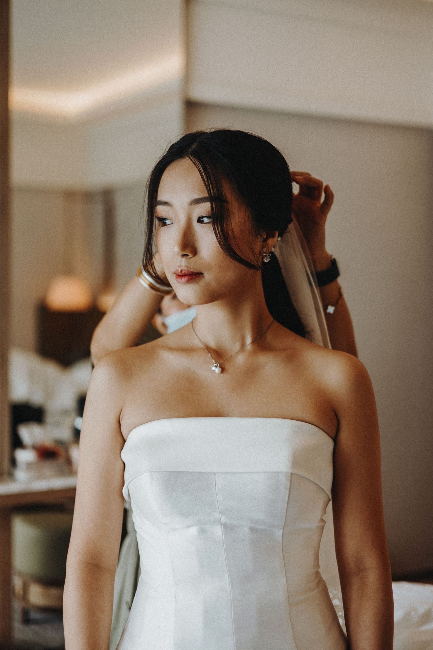 A bride wearing a strapless white wedding dress gets ready in an elegant indoor setting.