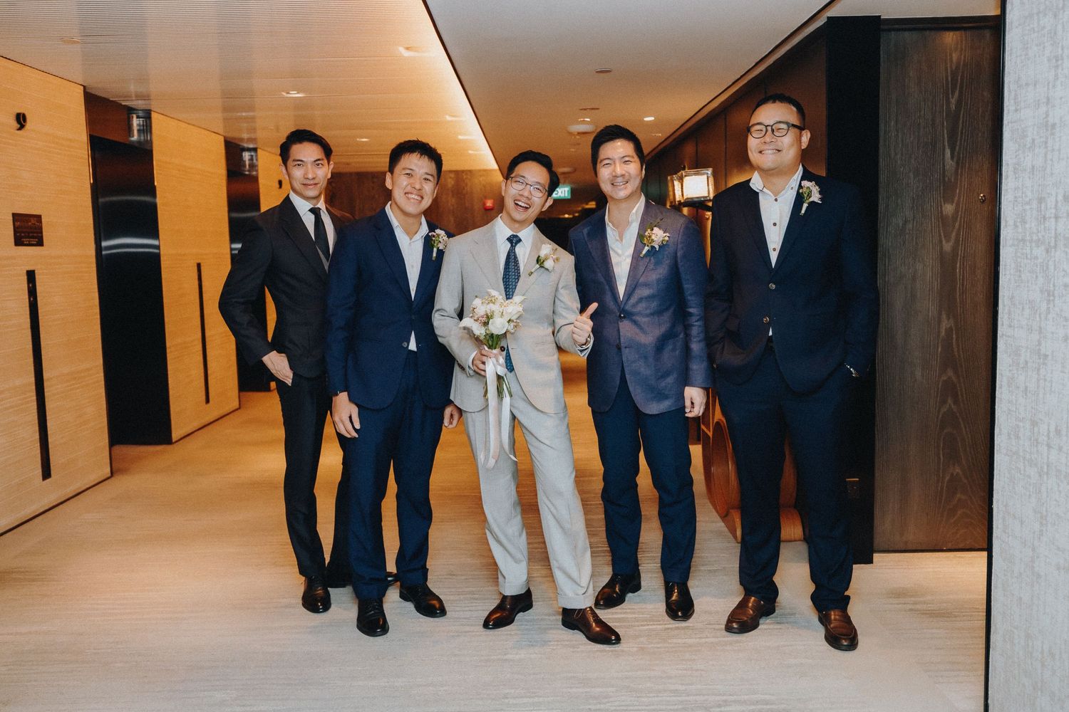 Wedding party in formal attire walking down a modern hallway together.