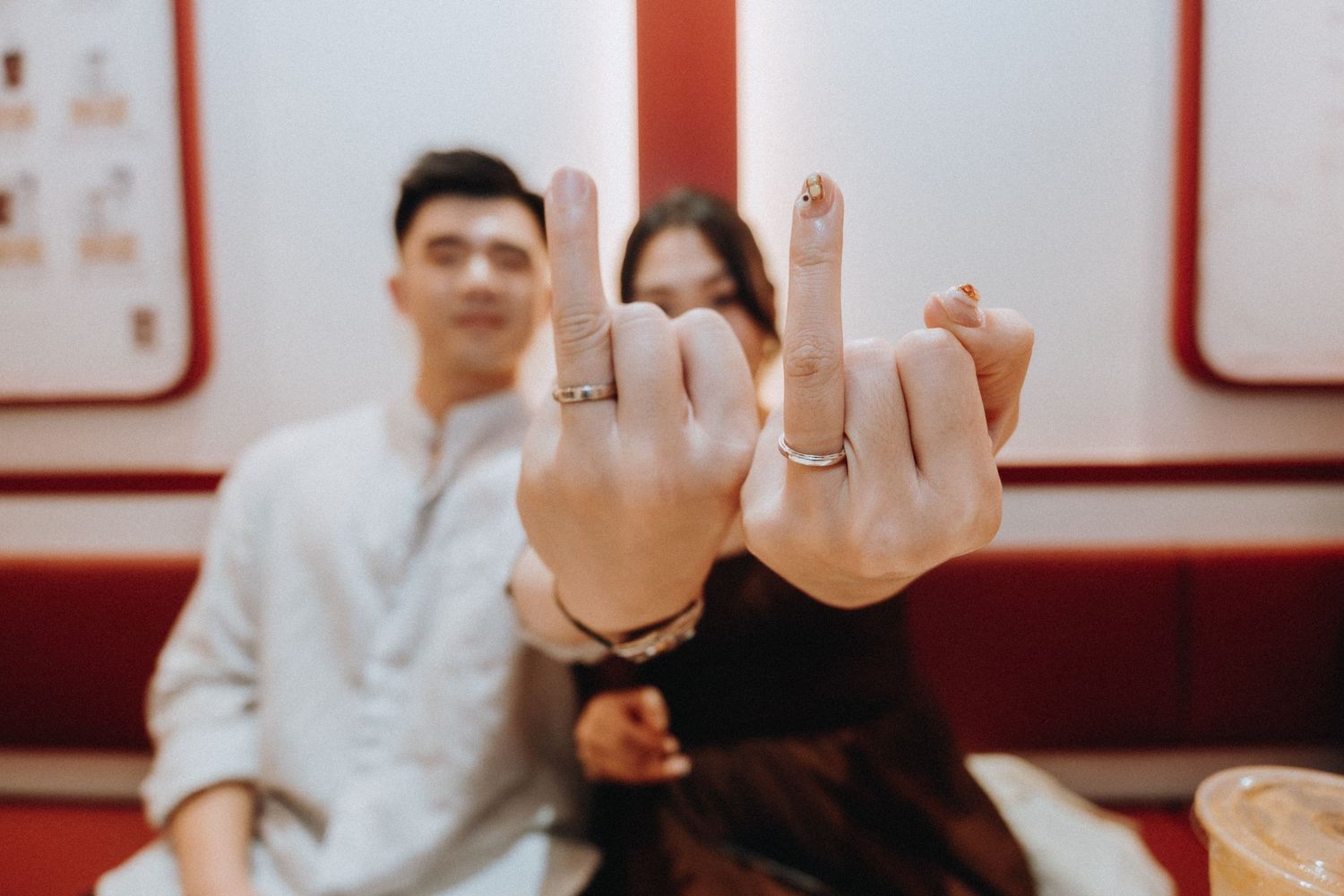 Couple showing off matching rings on their fingers, sitting together in a red and white interior setting.