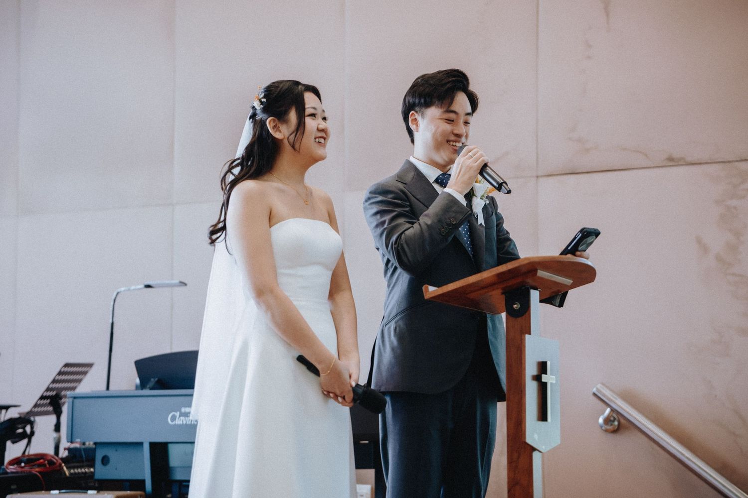 Bride and groom holding hands while groom speaks at church podium.