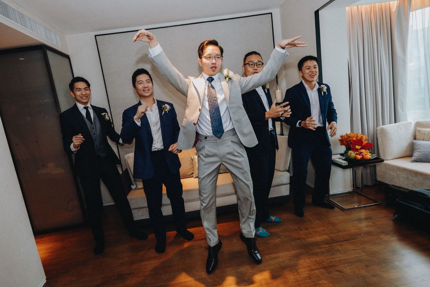 Wedding party members jumping and celebrating in a bright indoor space.